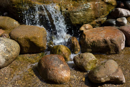 A mountain stream pours on the stones. Waterfall in the river. Rapids on the stream. The stones are wet with water. Beautiful background of a waterfall.の写真素材