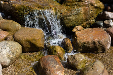 A mountain stream pours on the stones. Waterfall in the river. Rapids on the stream. The stones are wet with water. Beautiful background of a waterfall.の写真素材