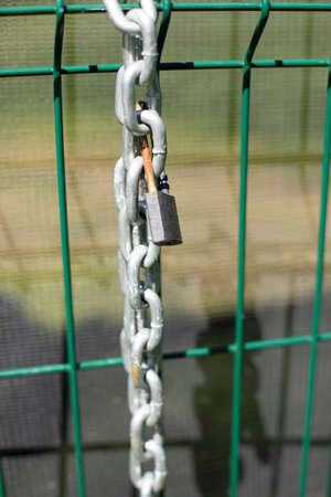 Chain on the fence. A metal chain hangs on the fence. Fence enclosing the territory with a lock and chain for blocking.の写真素材