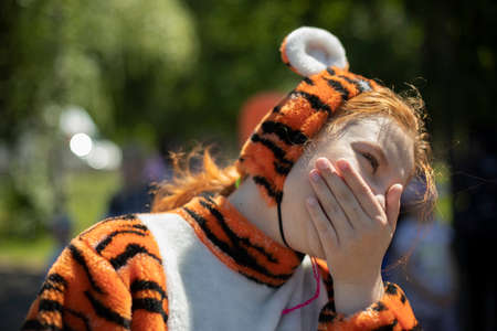 A girl dressed as a tiger. Children's animotr in a soft costume of a wild cat. A cute girl with red hair dressed in a cheerful outfit.の写真素材