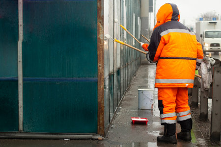 The painter paints with white paint. Paints graffiti with paint. Painting the wall. A worker paints over a vandalist inscription.の写真素材