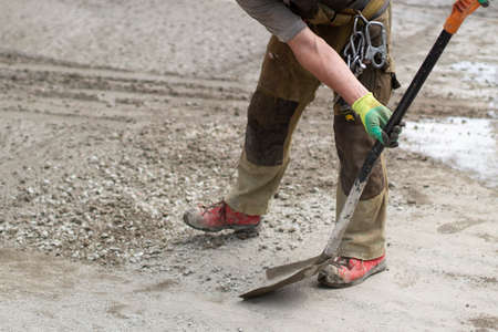 Work with a shovel at a construction site. A worker throws cement and gravel with a shovel. Cleaning the road from scattered building material.の写真素材