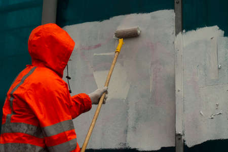 The painter paints with white paint. Paints graffiti with paint. Painting the wall. A worker paints over a vandalist inscription.の写真素材