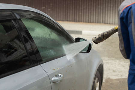 Car wash. The car is washed under the pressure of a jet of water. Using a water spray to wash off dirt from the surface of the car.の写真素材