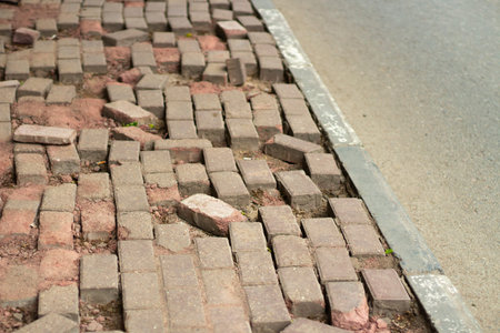 Broken paving stones on the road. The masonry is broken. The pedestrian road is destroyed. Poorly paved cobbled road. The tiles by the road shattered.の写真素材