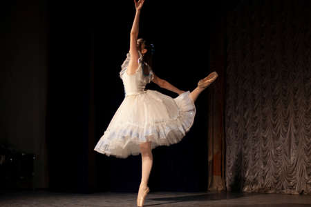 The girl is dancing on stage in a white dress. The artist is performing. Beautiful dance moves. Dance lesson for girls.の写真素材