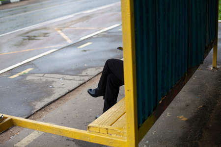 The man at the bus stop. Legs of a man who is waiting for the bus. Anonymous person. An unknown man is hidden behind a wall.の写真素材