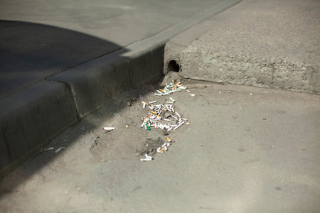 A pipe for draining water from the road. Clogged pipe on the side. Cigarette butts accumulate at the...