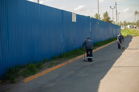 Road cleaner. The janitor sweeps the area with a broom. Removing garbage from the road. Putting things in order near the fence. Cleaning in the parking lot. The cleaner is working.の写真素材