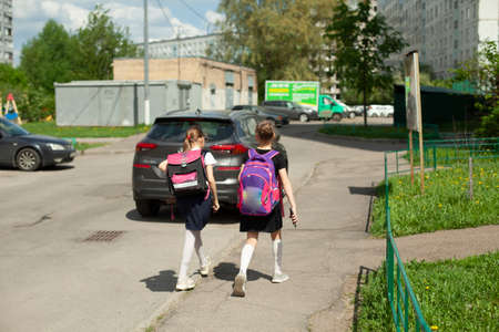 Two schoolgirls go home with backpacks. The girls walk down the street after school. Schoolgirls in Russia. Younger schoolgirls rush to school.の写真素材