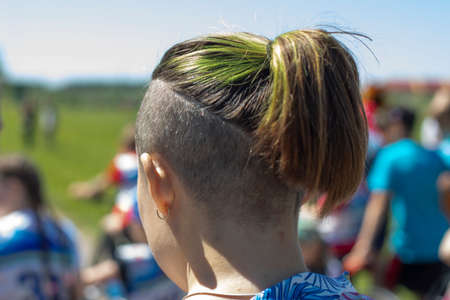 Shaved whiskey and green hair. Modern female hairstyle. Hair is pulled back in a ponytail. Green hair dye. Partially shaved head. The man is filmed from the back of his head.の写真素材