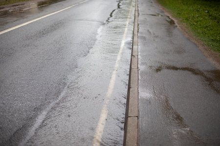 A meadow on a dart. The side of the road is flooded with rain. A lot of water flows along the road.の写真素材