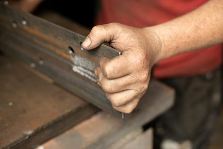 Drilled holes in the metal. Work in a metal workshop. The hand holds a steel blank. A man works in the garage.の写真素材