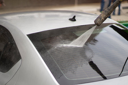 Car wash. The car is washed under the pressure of a jet of water. Using a water spray to wash off dirt from the surface of the car.の写真素材