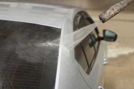 Car wash. The car is washed under the pressure of a jet of water. Using a water spray to wash off dirt from the surface of the car.の写真素材