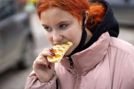 The girl eats flour. The girl is eating a sweet cake on the street. Delicious food outside the home. Hot baked goods in the hand of a teenager.の写真素材