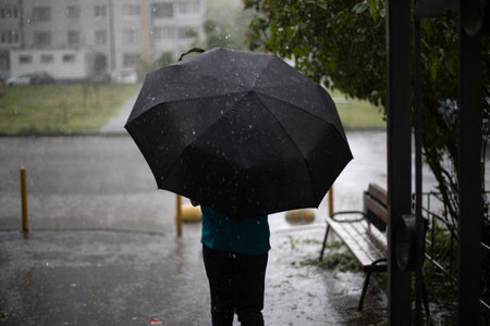 A man with an umbrella under a downpour. A passerby hides from the rain under an umbrella. Rainy weather outside.の写真素材