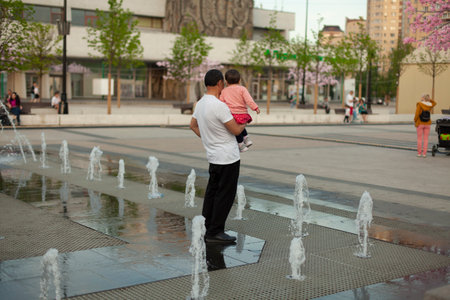 Dad with a child in his arms near the fountain. Father and daughter are resting at the city fountain. Father's family joy. The child is in the arms of a man.の写真素材