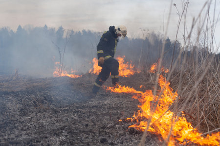 A firefighter extinguishes dry grass. A firefighter is fighting a fire in an open area. Rescuer...