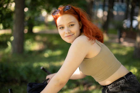Portrait of a girl on a bicycle. The girl looks into the camera. Summer holidays in the city. Red-haired teenage girl.の写真素材