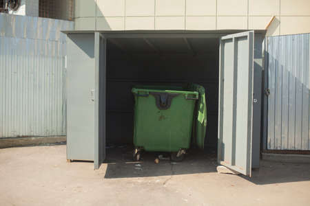 Trash can. Waste container in a fenced-in area. Collection of waste from the store. Garbage removal. Plastic container on wheels.の写真素材