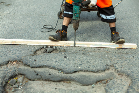 Removing the asphalt layer from the road. The worker holds a jackhammer. Road repair. Using an...