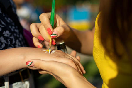 Draws a flower on her hand. The girl draws a flower to the child. Application of paint with a brush.の写真素材