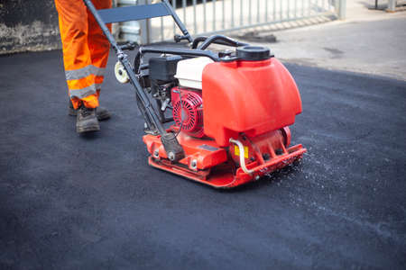 Asphalt laying. Leveling the road. A worker compresses warm asphalt. Road surface repair.の写真素材