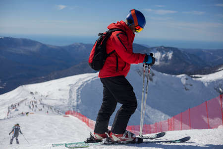 A skier rides on a snowy slope. Active rest in the winter. The athlete is preparing for the descent. Mountain ski resort. Outdoor activities on a winter vacation. The best time of the season. Man in a suit protecting from snow.の写真素材