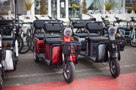 Moto electric vehicles are in a row. Electric bike rental. Headlights at two wheeled vehicles. Motorcycle sale. Mass parking of vehicles. Modern urban way of driving.の写真素材