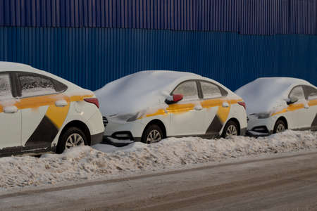 Taxis are parked on the roadside in winter. Snow-covered cars. Identical cars are parked in a row. Transport at a fine parking lot. Abandoned car sharing.の写真素材