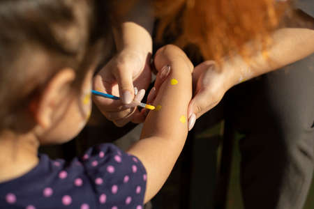 Draws with paint on his hand. Brush with paint for leather. The girl draws a picture to the child on the skin.の写真素材