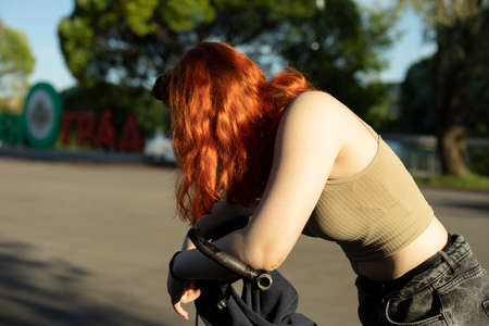 A girl on a bicycle in a tight T-shirt. A girl with red hair. Walk in the summer by bike. School is tired of the heat. Sunlight on a woman's shoulder and hair.の写真素材