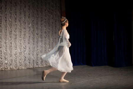 The girl dances in a classic dance dress. The performance of a young ballerina. The artist shows a scene with a dance.の写真素材