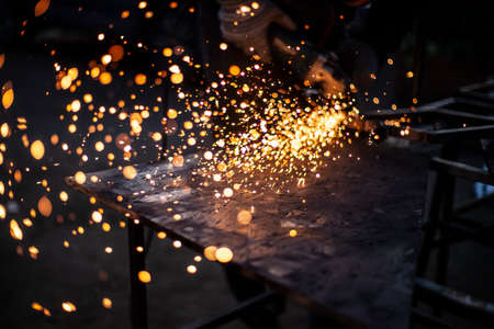 Metal processing in the workshop. Grinding metal. The worker makes the structure of a metal profile. Creating a shelving for the city dweller. Sparks from metal friction.の写真素材