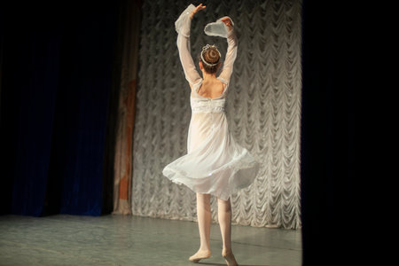 The girl is dancing on stage in a white dress. The artist is performing. Beautiful dance moves. Dance lesson for girls.の写真素材