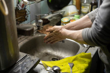 Hand washing in the sink. The bachelor washes his fingers with soap. Dirty sink in the house. Water pours from the tap.の写真素材