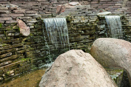 Artificial waterfall. Water runs over the stones. Landscaping in the park.の写真素材