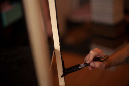 A girl paints furniture at home. Painting with a brush in the black color of a wooden surface. Brush in the girl's hand.の写真素材
