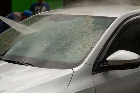 Car wash. The car is washed under the pressure of a jet of water. Using a water spray to wash off dirt from the surface of the car.の写真素材