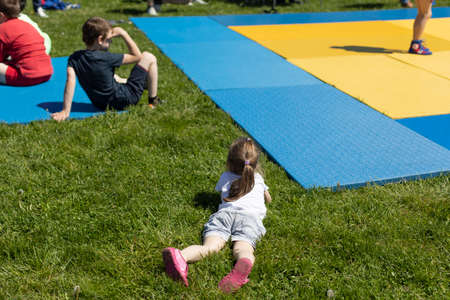 The child is lying on the grass. A girl at a sporting event. Rebekah rests in the park in the summer. The kids are watching the tournament.の写真素材