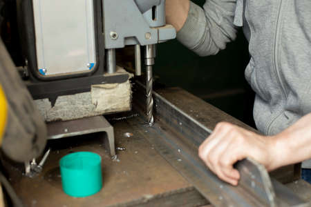 The guy's drilling steel. Metal drilling machine. Hard work in a metal workshop. The hand holds a steel blank.の写真素材