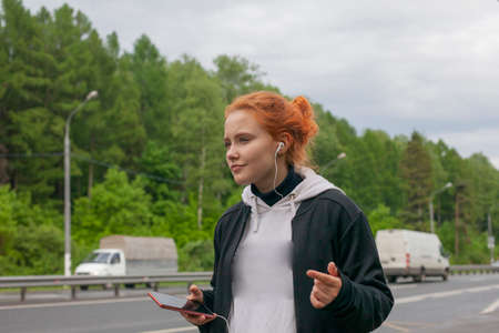 Teenager on the street. The girl is waiting for the bus. An ordinary child. The girl listens to headphones.の写真素材