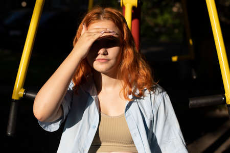 Girl on the playground. A friend is sitting on the simulator. Walk in the yard. Bright light. Rest on a hot day.の写真素材