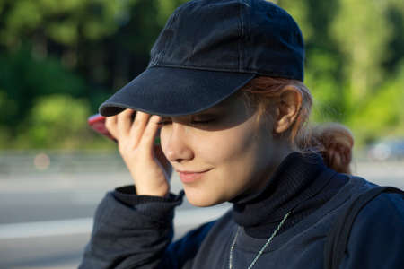 The girl listens to the message from the smartphone. The teenager speaks on the phone in the street. The girl communicates on the Internet in the summer.の写真素材