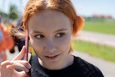 The girl speaks on the phone. A teenager is talking on a smartphone. The girl talks emotionally. The teenager holds a smartphone near the ear.の写真素材