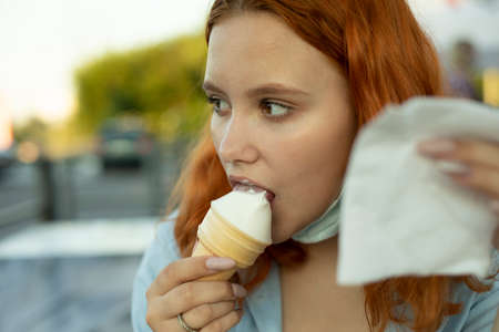 The girl is eating vanilla ice cream. Girl bites a waffle cone in summer. A cold treat in the heat in the hand of a teenager.の写真素材