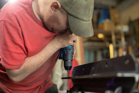 A man drills holes in the metal. The guy works in the garage. Hard man's work. Drilling holes a blank.の写真素材