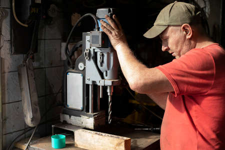 A man installs a drilling machine. The guy in the workshop is setting up the equipment. A machine for making holes in metal.の写真素材