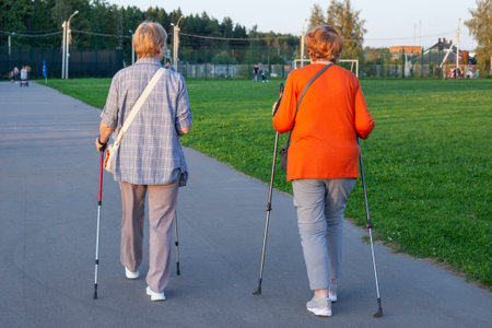 Nordic walking with sticks. Pensioners take care of their health. Evening walk along the street. Grandmothers train muscles. Women are walking in the park. Walking with sticks for a beautiful posture.の写真素材